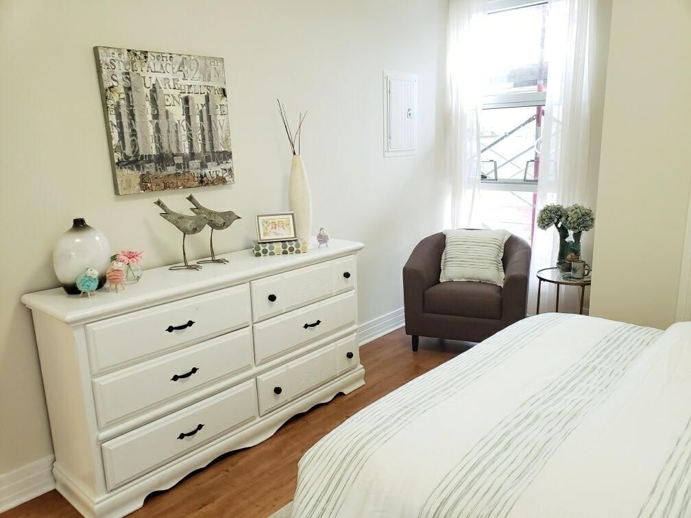 A bright and airy bedroom featuring a white dresser, cozy armchair, and minimalist decor.