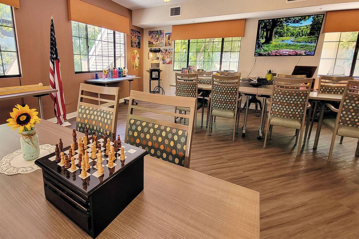 A cozy community room featuring a chess board, tables, chairs, and a television.