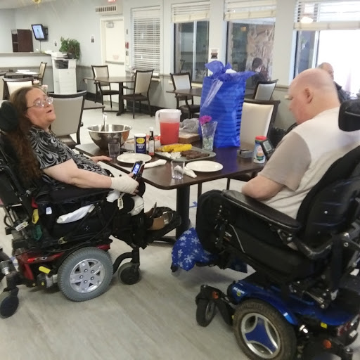 Two individuals in wheelchairs enjoying a meal together in a dining area.