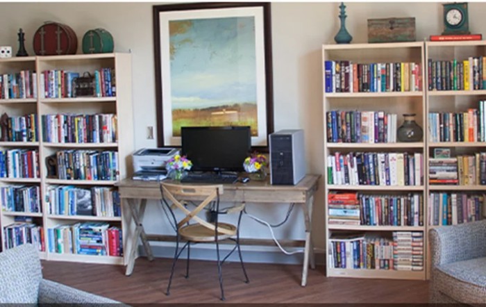 A cozy home office setup with a computer desk surrounded by bookshelves and a large painting on the wall.