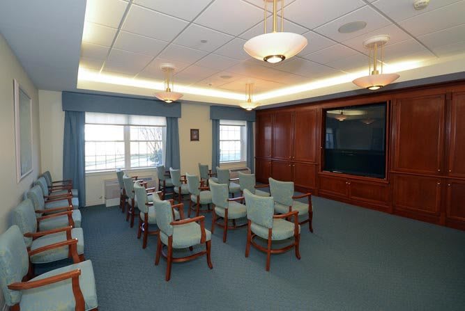 A well-furnished conference room with multiple chairs around a table, featuring wood paneling and large windows.