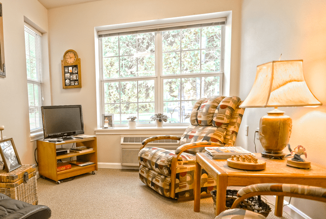 A cozy living room with a comfortable armchair, television, and large window allowing natural light.
