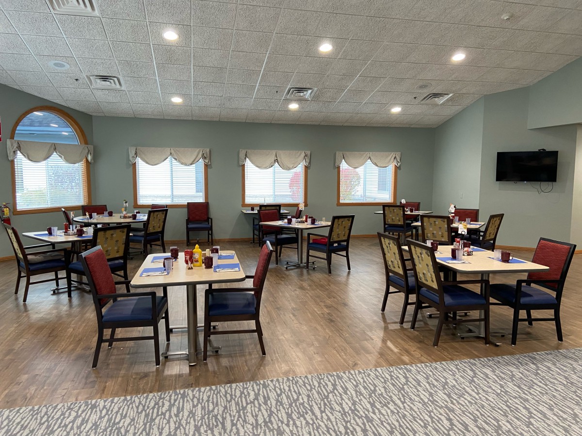 A cozy dining room with neatly arranged tables and chairs, featuring soft lighting and simple decor.