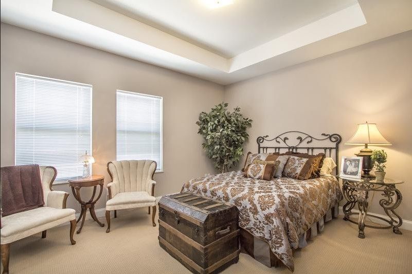 A cozy bedroom with vintage decor, featuring an elegant armchair and a classic trunk at the foot of the bed.