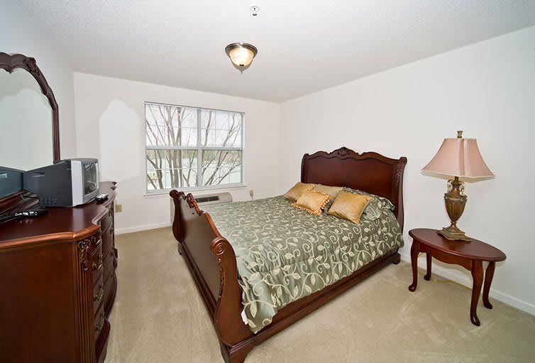 A cozy bedroom with a wooden bed, dresser, and a window letting in natural light.