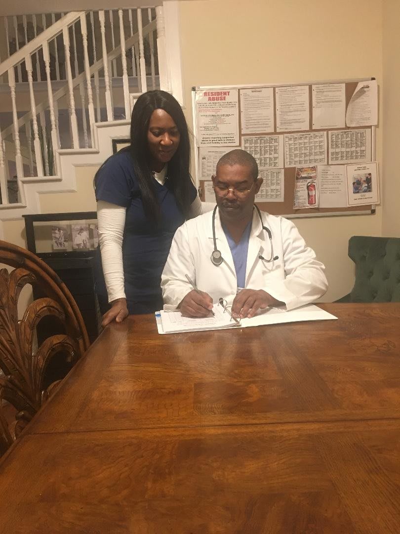 A medical professional sitting at a desk with a stethoscope, accompanied by a woman standing beside him.