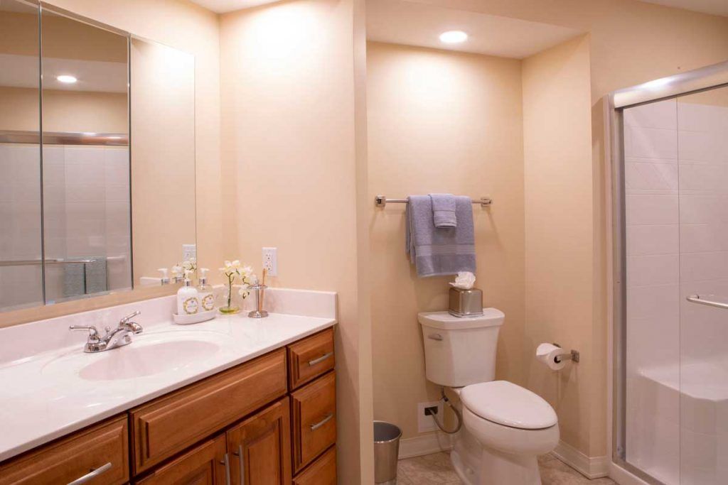 A clean and organized bathroom with a sink, mirror, and toilet featuring neutral tones and simple decor.