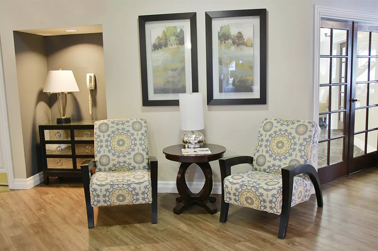 A cozy living room setup with two patterned chairs flanking a small round table, accompanied by framed artwork on the wall.