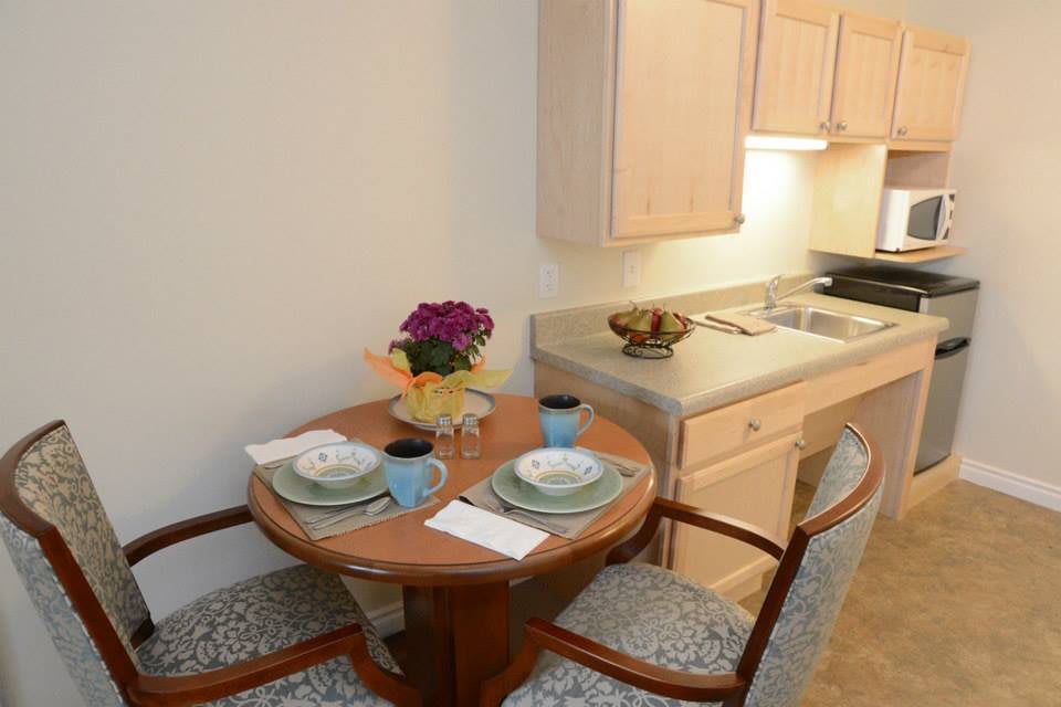 A cozy kitchenette with a small dining setup featuring two chairs, plates, and flowers.