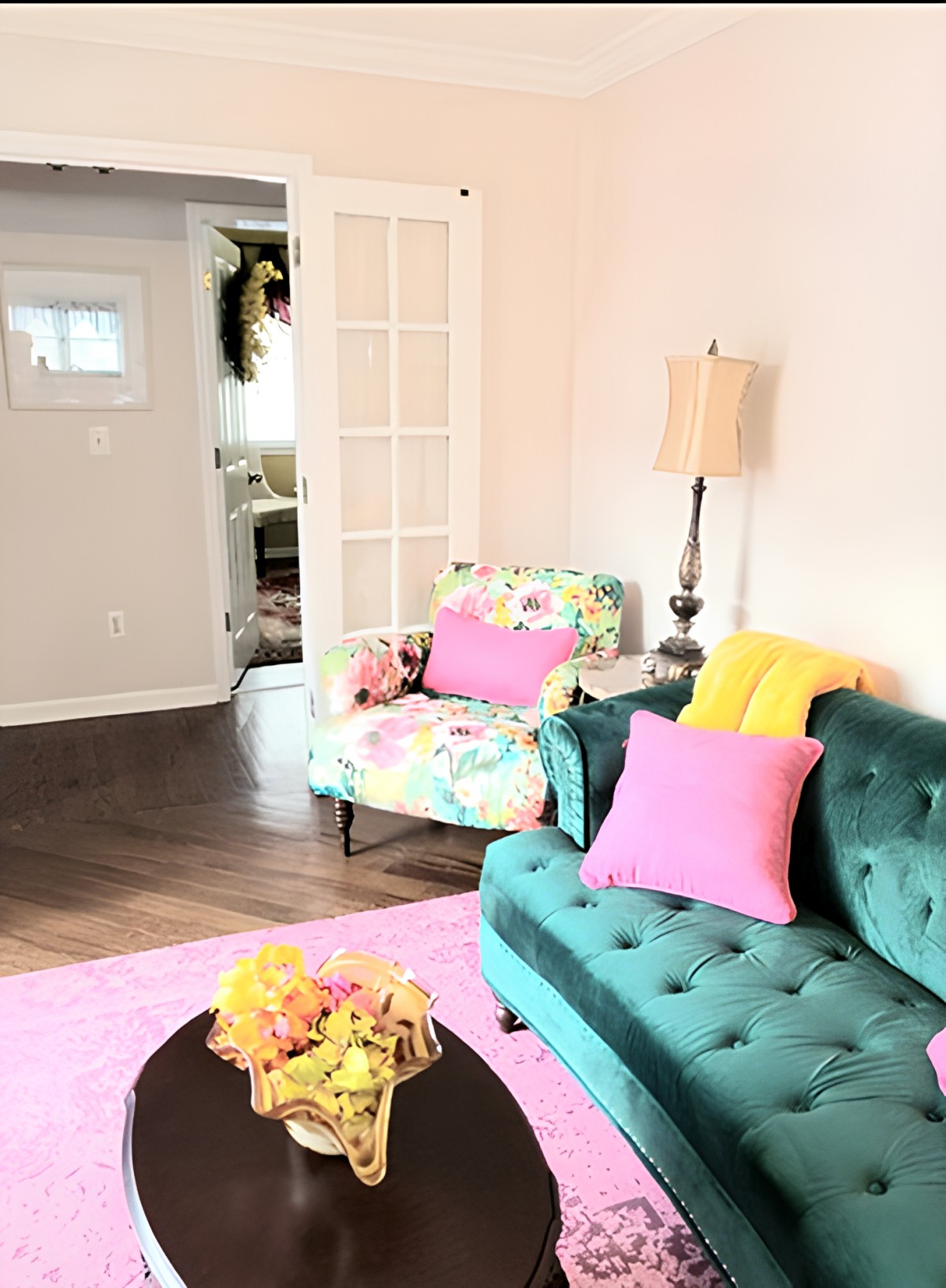 A bright and colorful living room featuring a teal sofa, a floral armchair, and vibrant pink pillows.