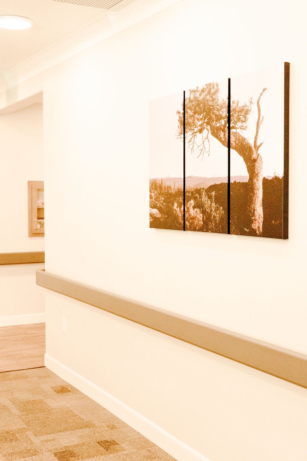 A hallway with a large tree painting on the wall, featuring warm tones and minimalist decor.