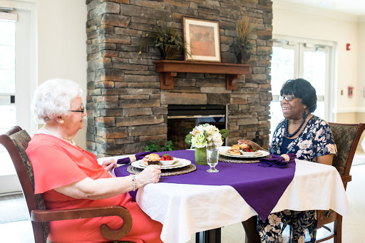 Two women enjoying a meal together at a beautifully set table, with a cozy stone fireplace in the background.