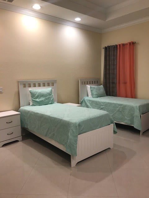 A cozy bedroom featuring twin beds with matching teal bedding, a nightstand, and colorful curtains.