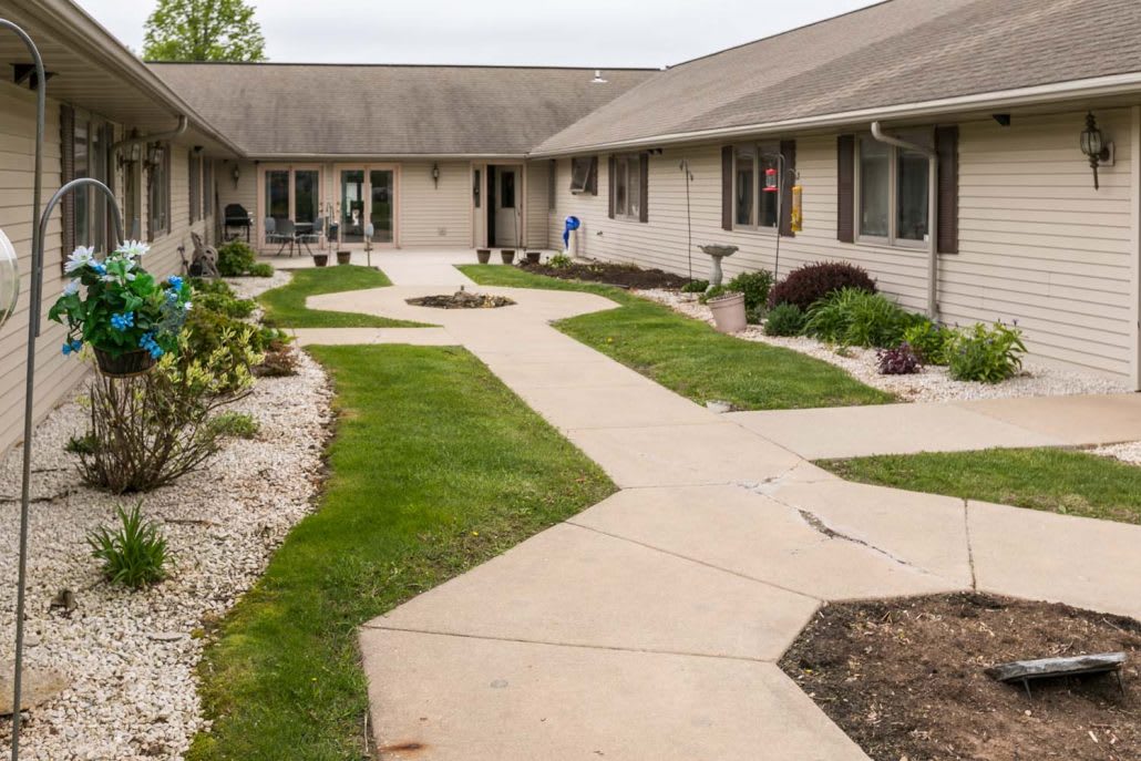 A landscaped courtyard with a paved walkway surrounded by grass and a single-story building.