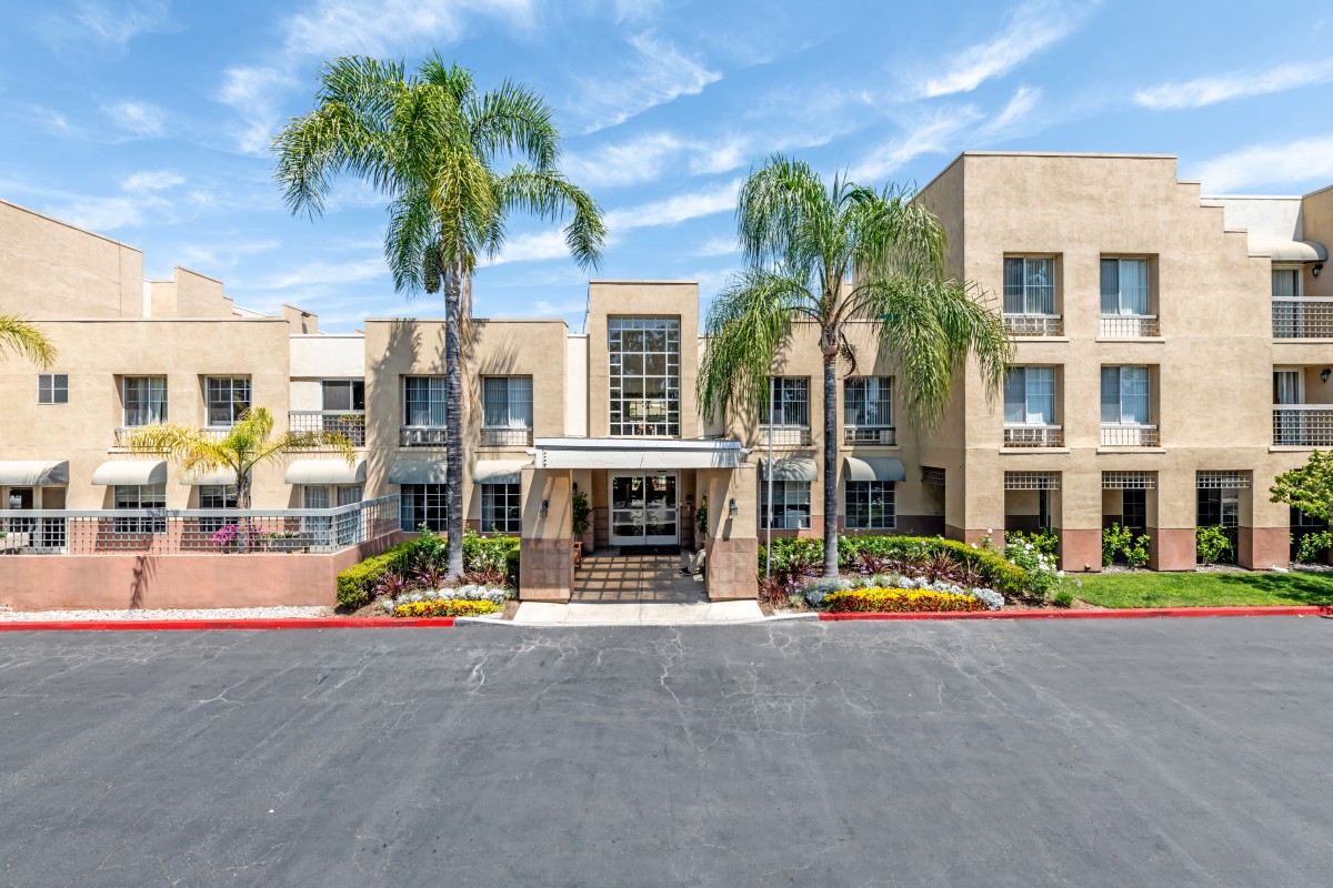 A modern building with palm trees and landscaped gardens on a sunny day.