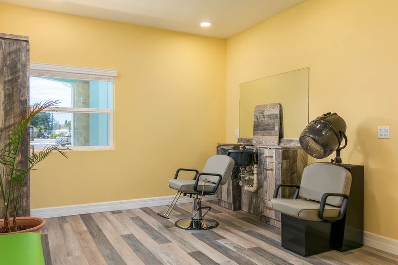 A cozy hair salon interior with yellow walls, equipped with chairs, a large mirror, and a hairdryer.