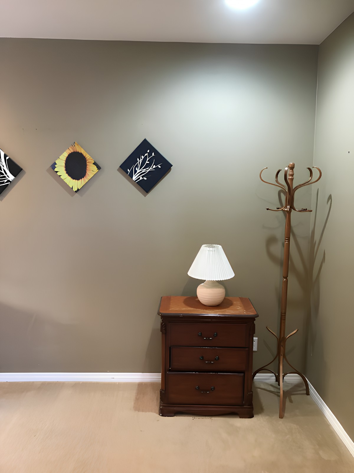 A cozy corner featuring wall art, a lamp on a wooden nightstand, and a coat rack.