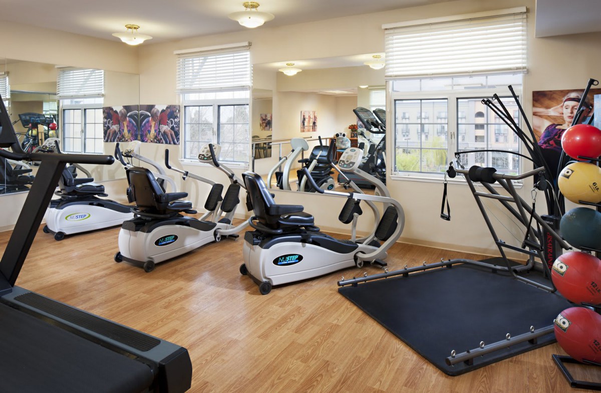A well-lit gym with various exercise equipment including treadmills and elliptical machines.