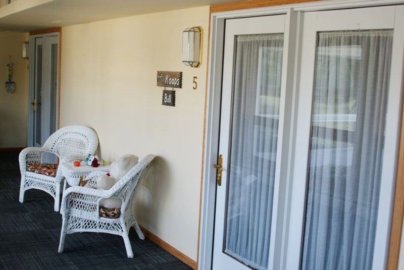 A cozy patio area featuring a wicker chair and table set, positioned near French doors with a wall-mounted light fixture and decorative elements.