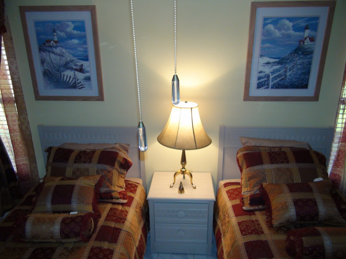 A cozy bedroom with twin beds, a central lamp on a nightstand, and paintings on the wall.
