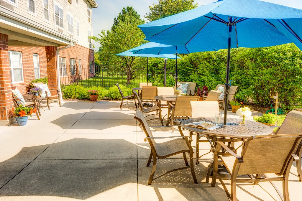 A sunny outdoor patio area with tables, chairs, and blue umbrellas beside a building.