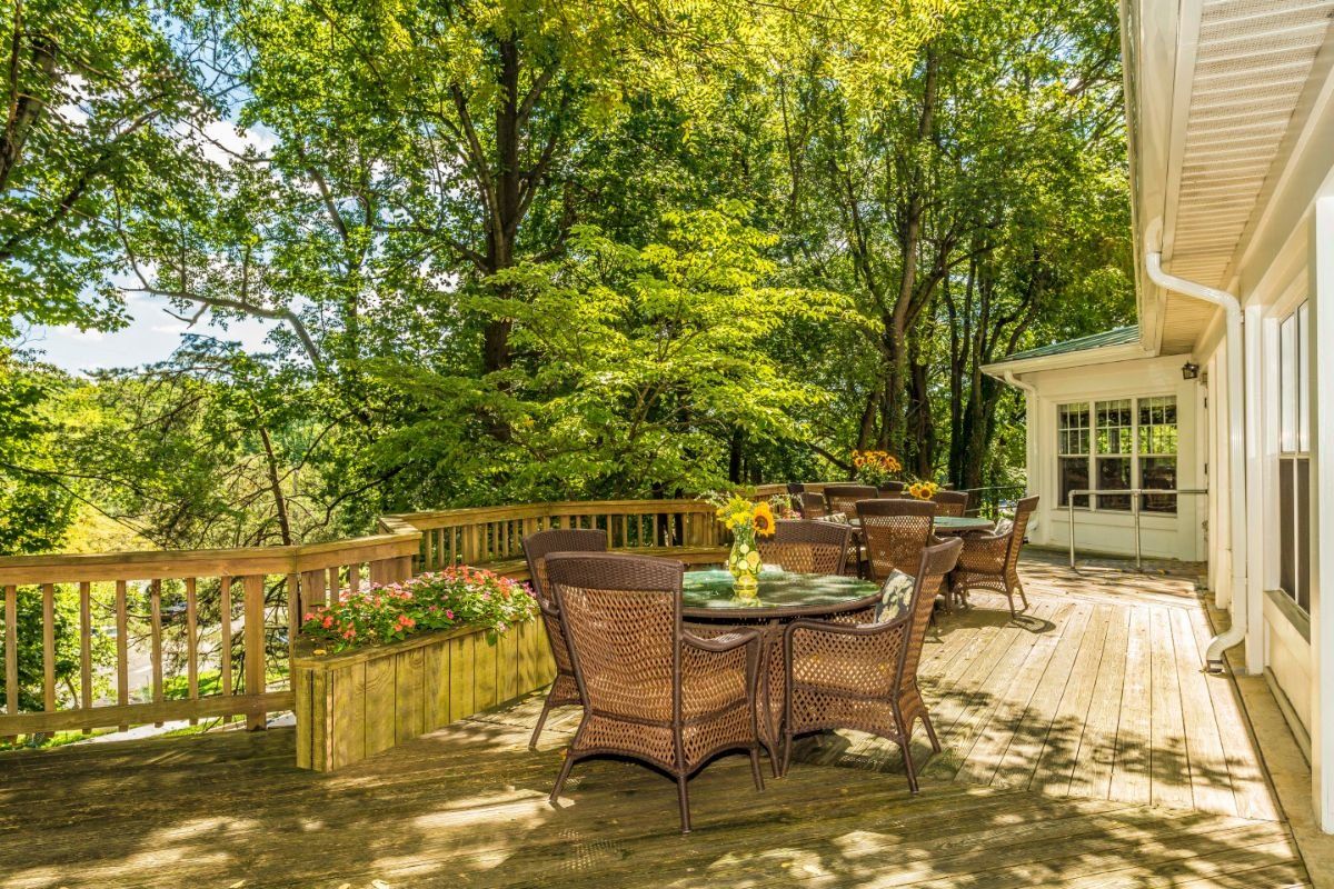 A sunny outdoor deck with wicker patio furniture surrounded by lush trees.