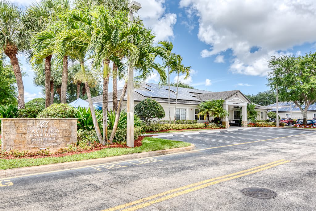 A sunny day view of a building surrounded by palm trees and clouds.