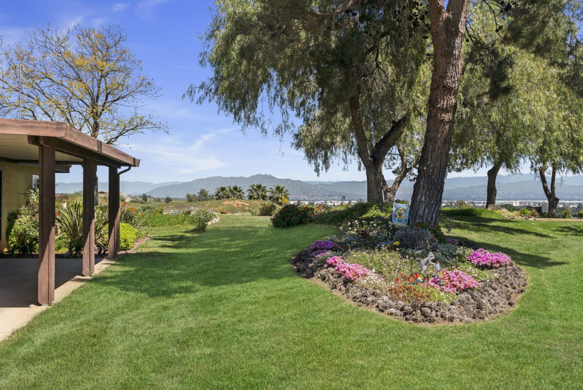 A beautifully landscaped garden with lush green grass, colorful flower beds, and tall trees under a clear blue sky.