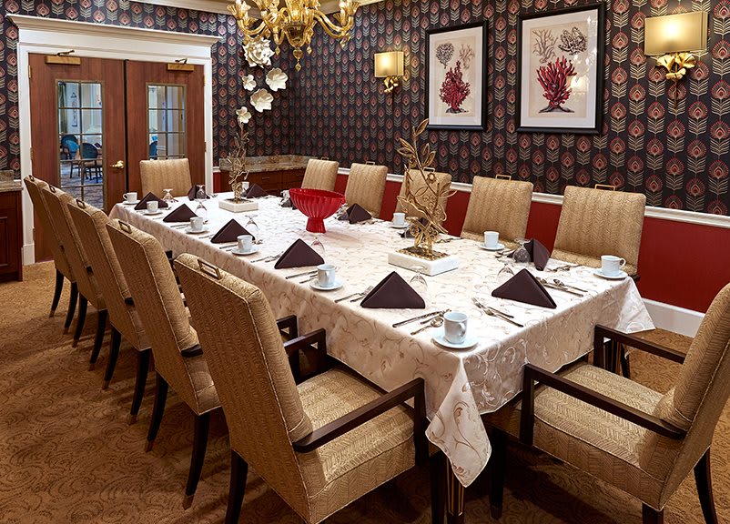 A formal dining room with an elegantly set table, featuring a chandelier and decorative wall art.