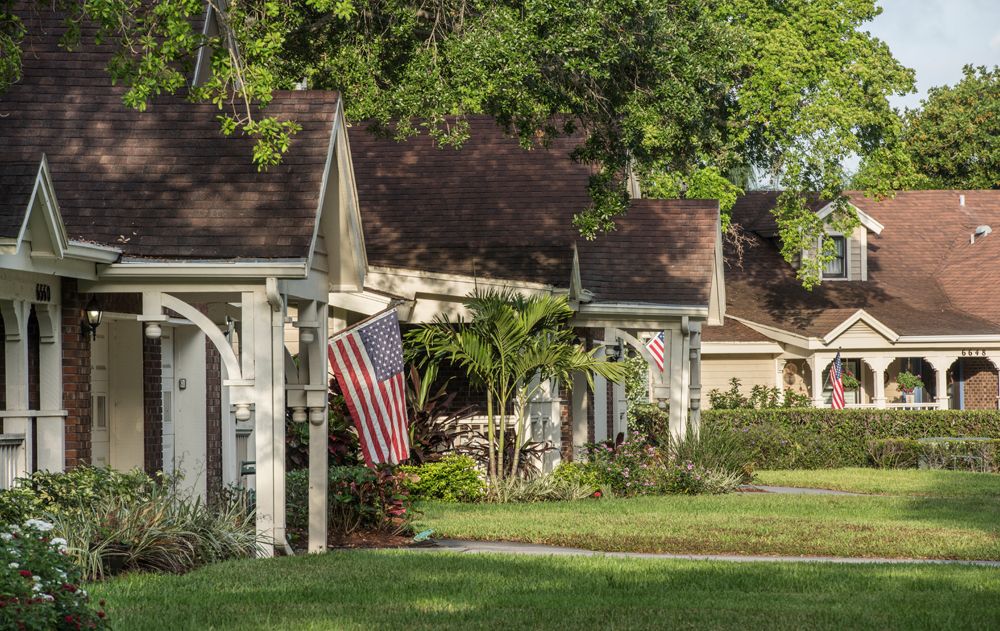 A suburban neighborhood with houses, an American flag, and lush greenery.