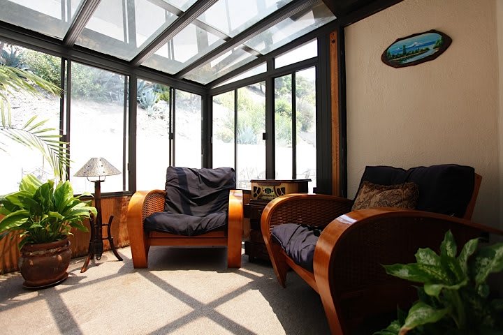A bright sunroom with wooden chairs and abundant natural light streaming through the glass roof.