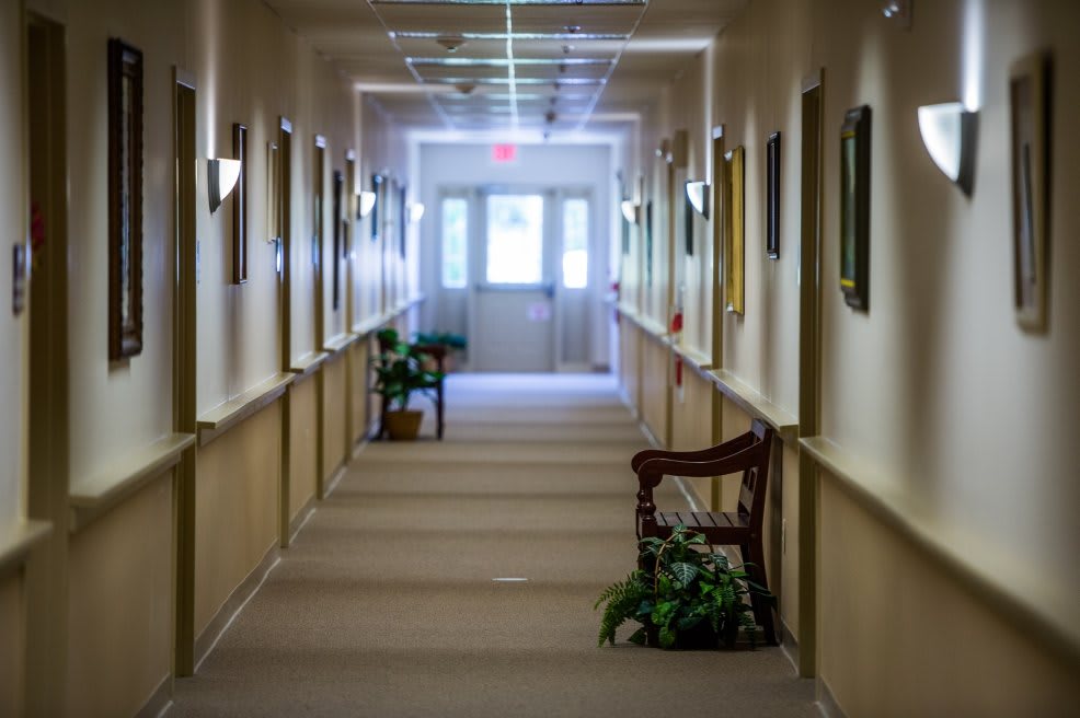 An empty hallway with carpeted floors, decorated with chairs and wall art, leading to a set of glass doors.