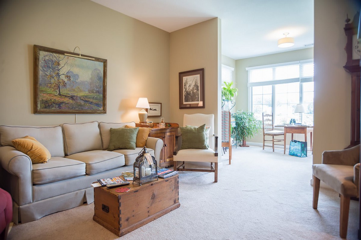 A cozy, well-lit living room featuring a comfortable sofa and wooden furniture, accented with artwork and decor pieces.