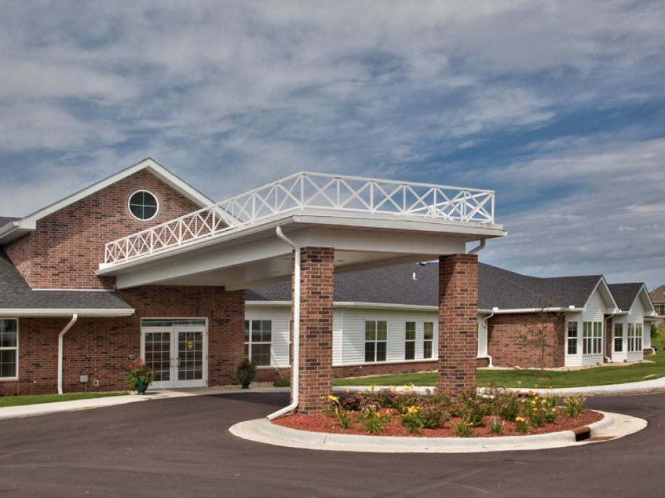 A brick building with a covered entrance and landscaped surroundings under a partly cloudy sky.
