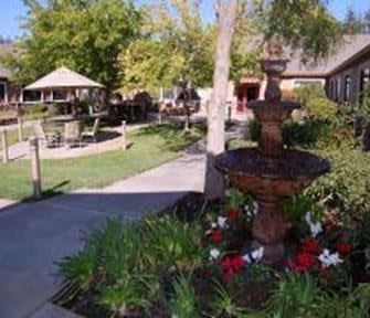 A serene garden featuring a fountain, pathway, and seating areas surrounded by lush greenery.