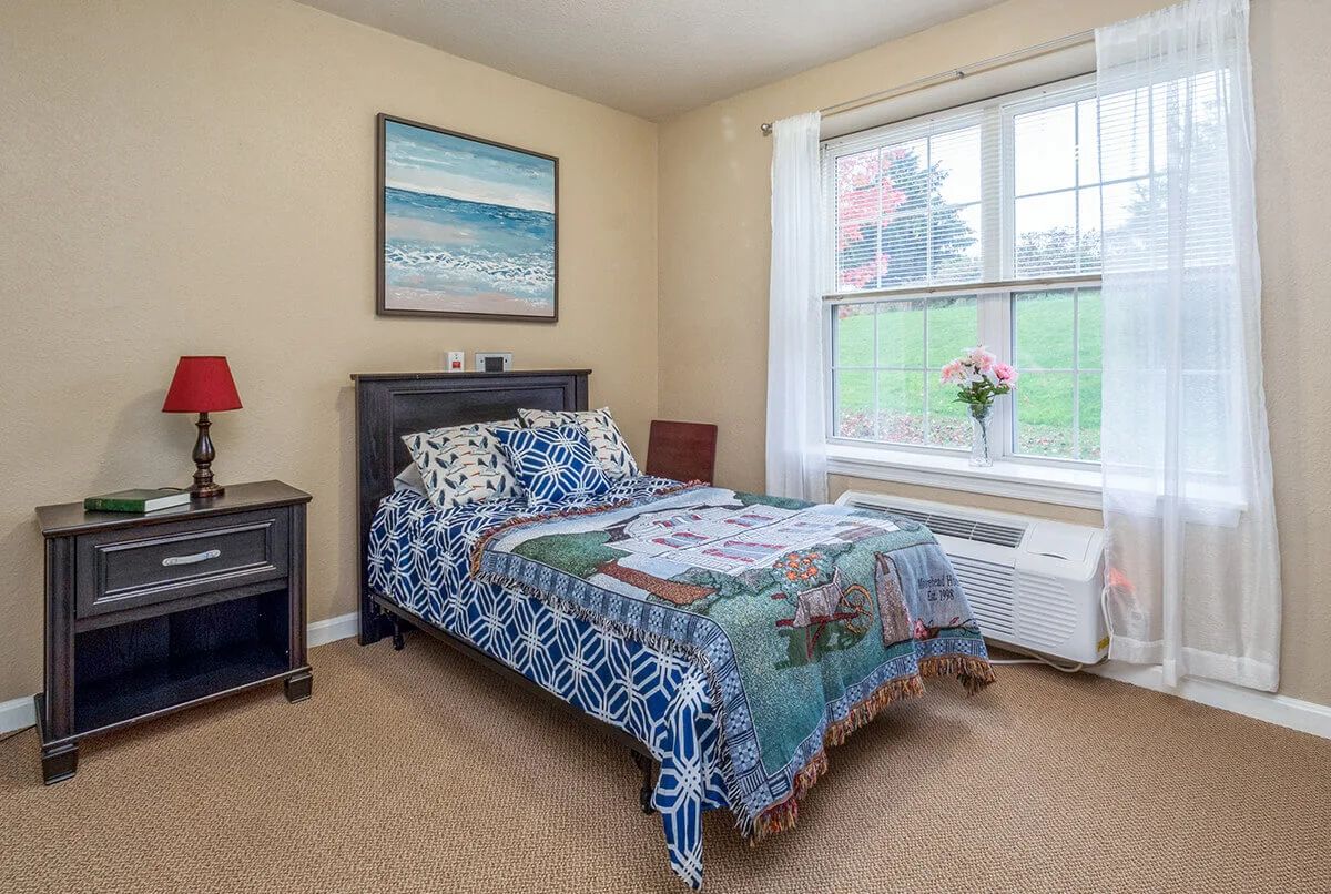 A cozy bedroom with a single bed, colorful bedding, and a large window bringing in natural light.