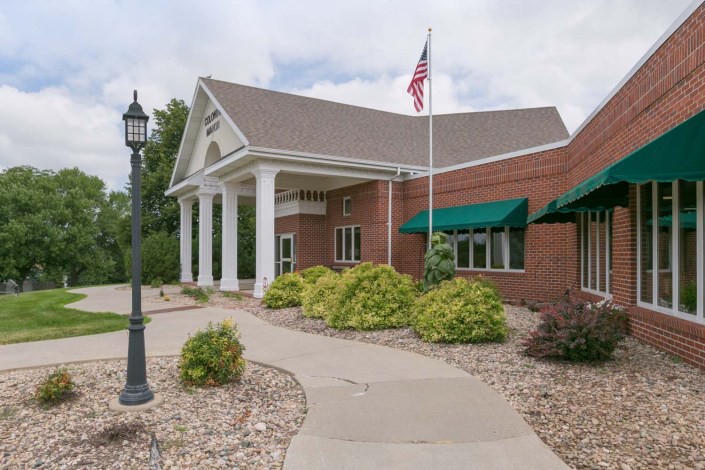 A brick building with white columns, green awnings, and an American flag.
