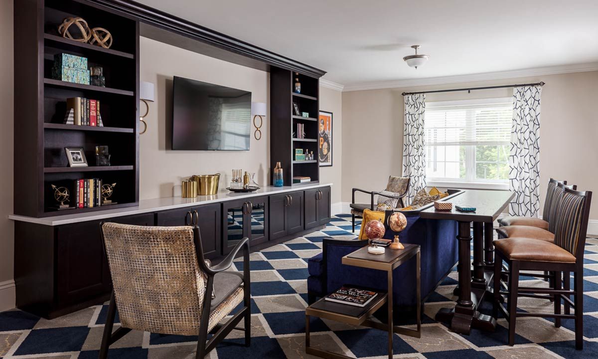 A modern living room featuring a large television, built-in shelves, and stylish armchairs with a geometric rug.