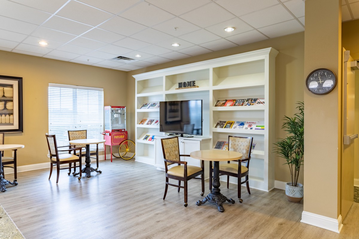 A cozy seating area with tables, chairs, and a large television set in front of built-in shelves.