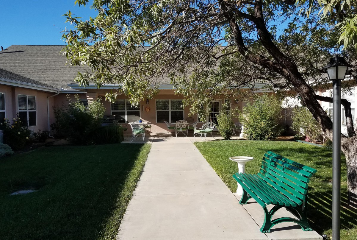 A serene garden view with a pathway leading to a house, flanked by trees and a green bench.