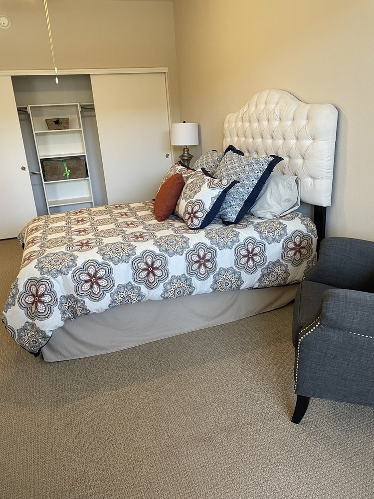 A well-decorated bedroom with a tufted headboard bed, patterned bedding, and a cozy chair.