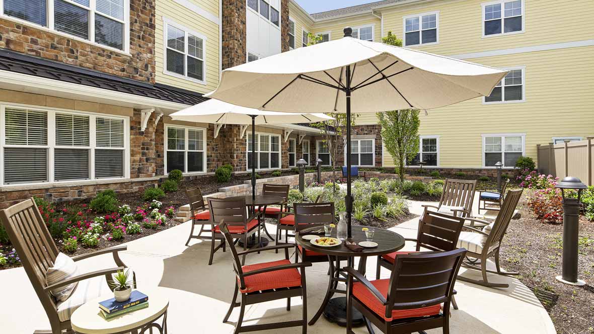A charming patio area with tables and chairs shaded by large umbrellas, situated outside a residential building.