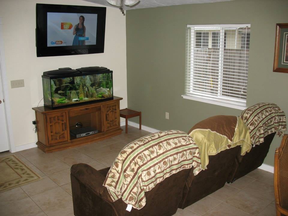 A cozy living room with a sofa, a fish tank, and a mounted TV, featuring blankets draped over the furniture.