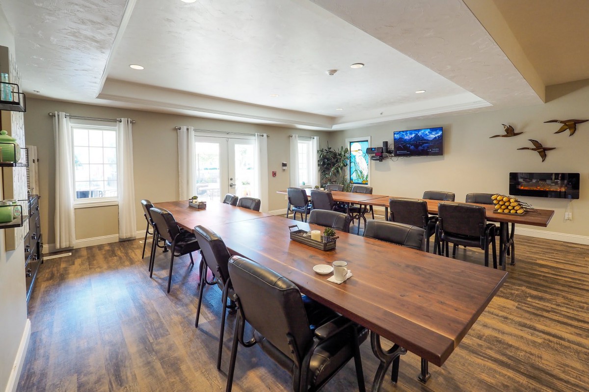 A modern conference room with a large wooden table, several chairs, and a television on the wall.
