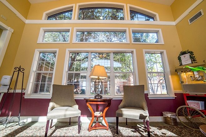 A cozy living room setting with two chairs and a lamp by large, sunlit windows.