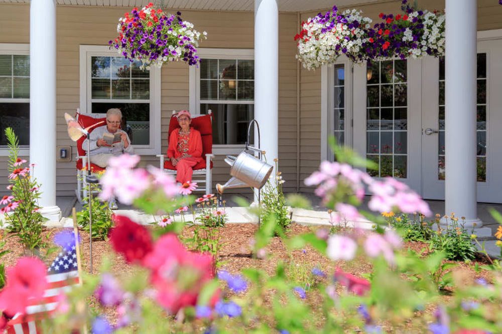 A colorful garden view with flowers and people relaxing on a porch.