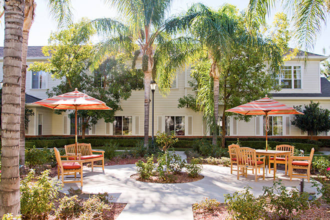 A peaceful outdoor patio area with seating and umbrellas, surrounded by palm trees and greenery.