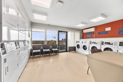 A modern laundry room featuring washing machines, dryers, and a comfortable waiting area with large windows.