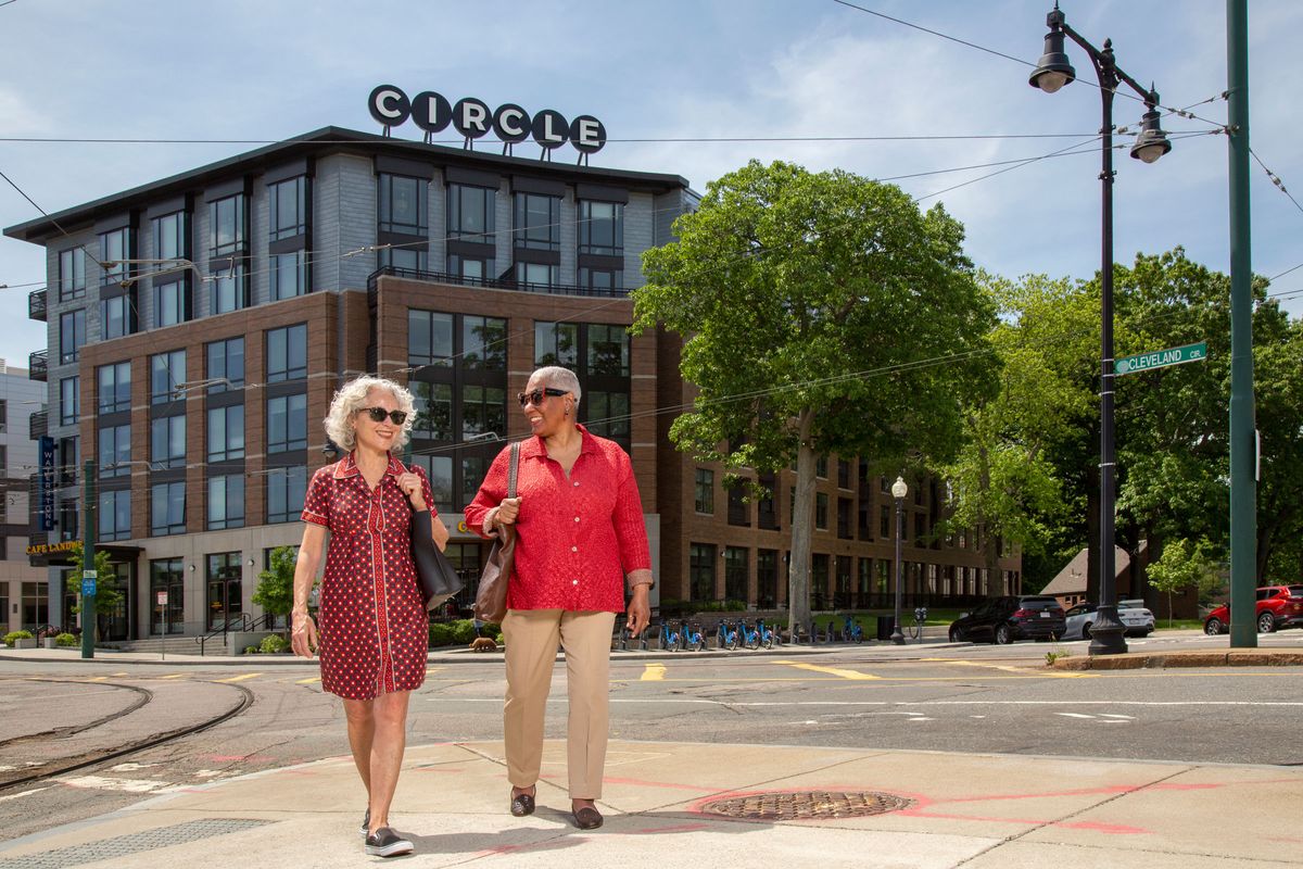 A couple strolling in an urban area with a modern building and trees in the background.