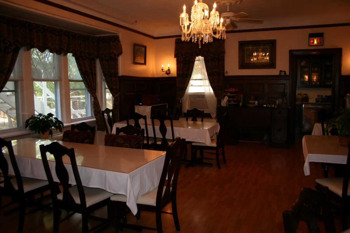 A cozy dining room with traditional decor, featuring a chandelier, wood furniture, and elegant curtains.